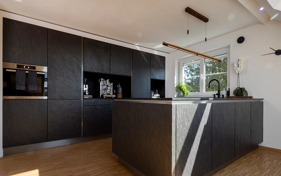 Moderne Küche mit Kochinsel, dunklen Fronten und klarer Linienführung, umgesetzt vom Küchenstudio Lorinser