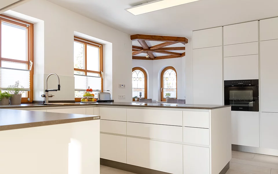 Moderne Küche mit weißen Fronten, Holzarbeitsplatte und offener Gestaltung, umgesetzt vom Küchenstudio Lorinser