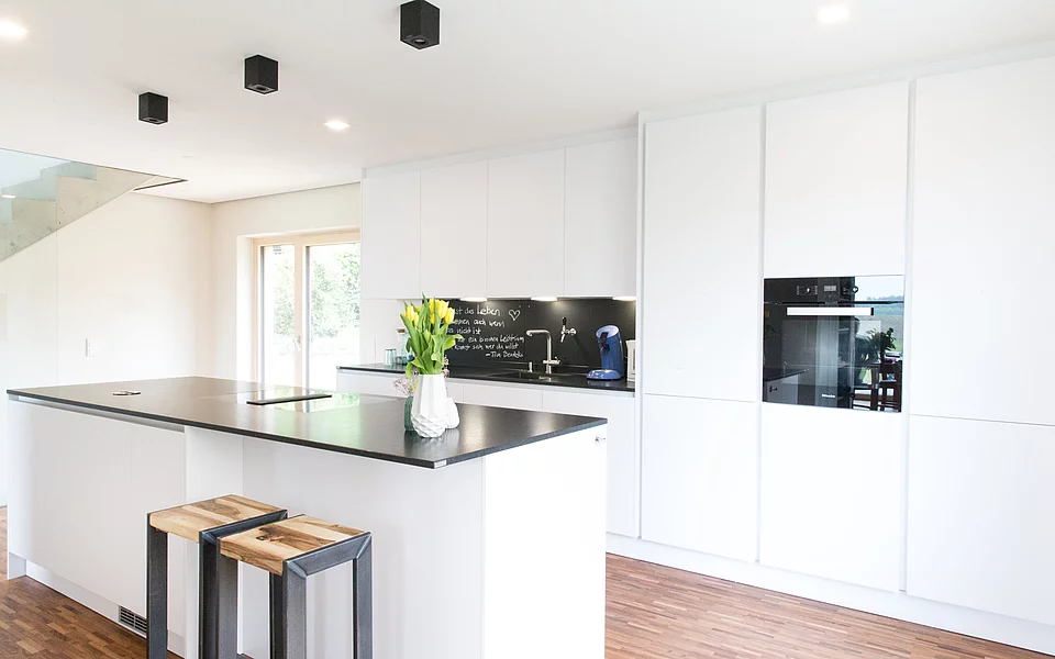 Helle Wohnküche mit weißen Fronten, offenen Regalen und minimalistischer Gestaltung, umgesetzt vom Küchenstudio Lorinser