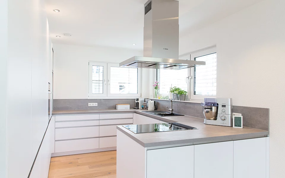 L-förmige Küche mit hellen Fronten und warmen Holzelementen, realisiert vom Küchenstudio Lorinser