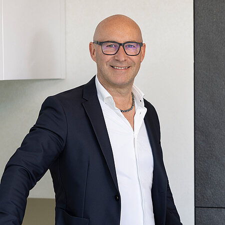 Mann im Anzug steht vor moderner Küche und lächelt, Mitarbeiter vom Küchenstudio Lorinser