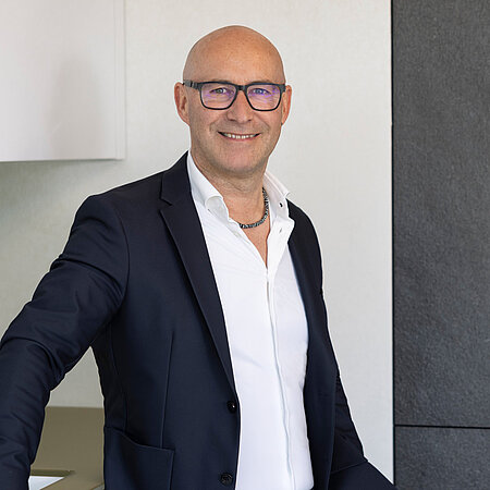 Mann im Anzug steht vor moderner Küche und lächelt, Mitarbeiter vom Küchenstudio Lorinser