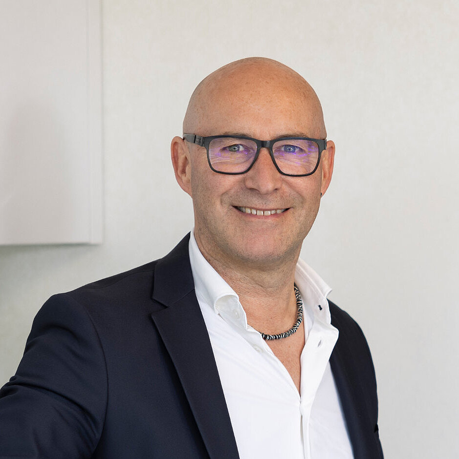 Mann im Anzug steht vor moderner Küche und lächelt, Mitarbeiter vom Küchenstudio Lorinser