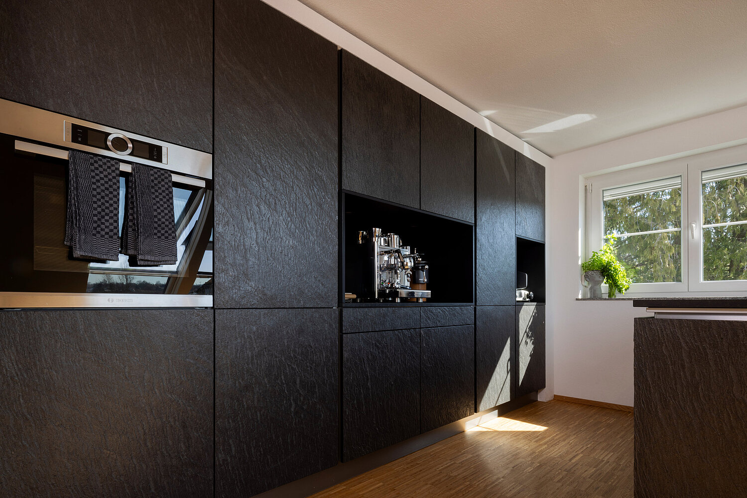 Moderne Küche mit dunklen Fronten, Kücheninsel und offenem Wohnbereich, umgesetzt vom Küchenstudio Lorinser