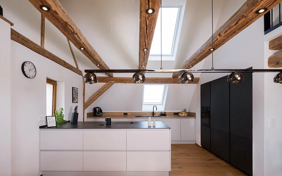 Moderne Küche unter Dachschräge mit offenen Balken und großzügiger Arbeitsfläche, umgesetzt vom Küchenstudio Lorinser
