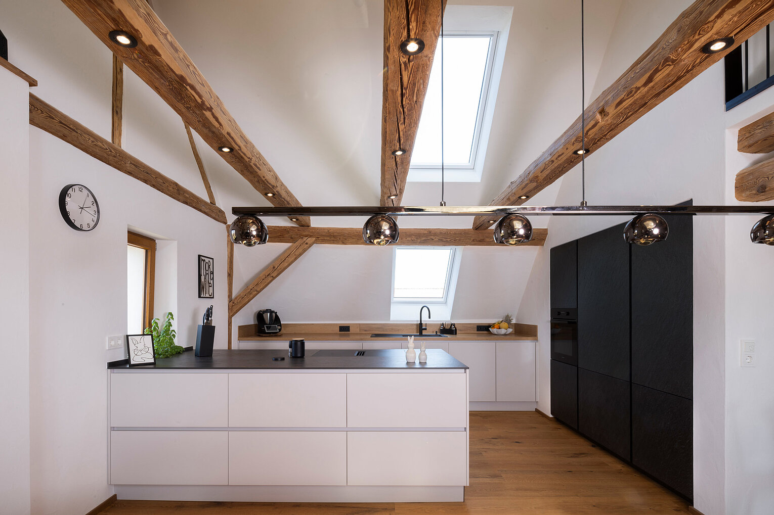 Moderne Küche unter Dachschräge mit offenen Balken und großzügiger Arbeitsfläche, umgesetzt vom Küchenstudio Lorinser