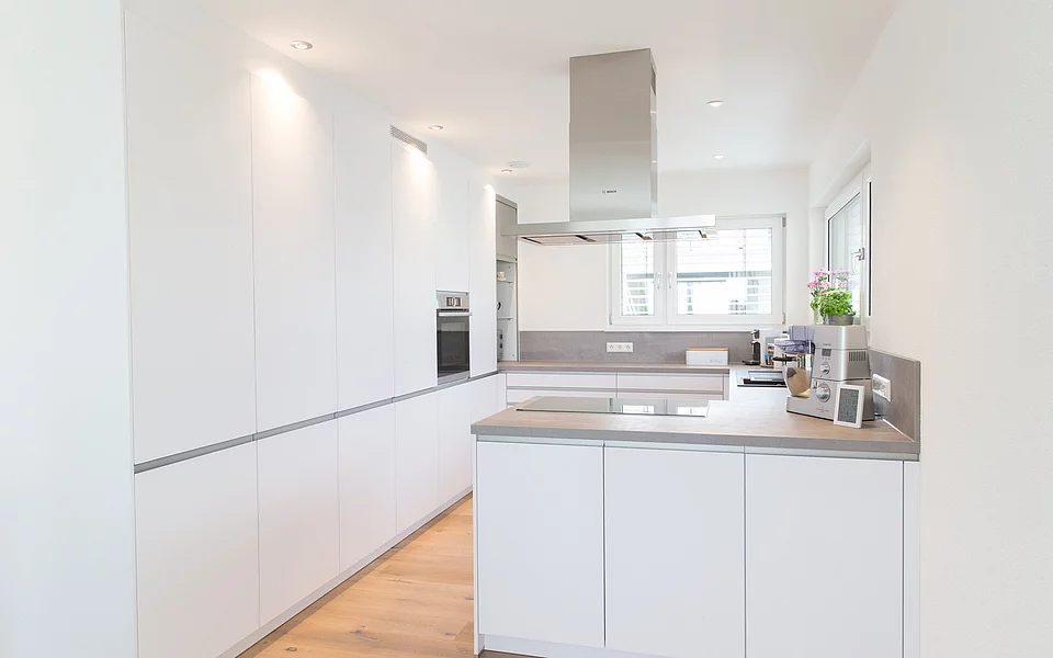 Moderne Küche mit weißen Fronten, Holzarbeitsplatte und klarer Struktur, umgesetzt vom Küchenstudio Lorinser