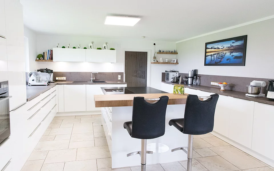 Offene Küche mit integriertem Arbeitsplatz und modernen Sitzmöglichkeiten, umgesetzt vom Küchenstudio Lorinser