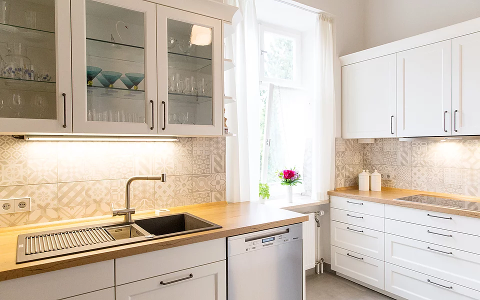 Moderne Küche mit weißen Fronten, Holzarbeitsplatte und viel Tageslicht, realisiert vom Küchenstudio Lorinser