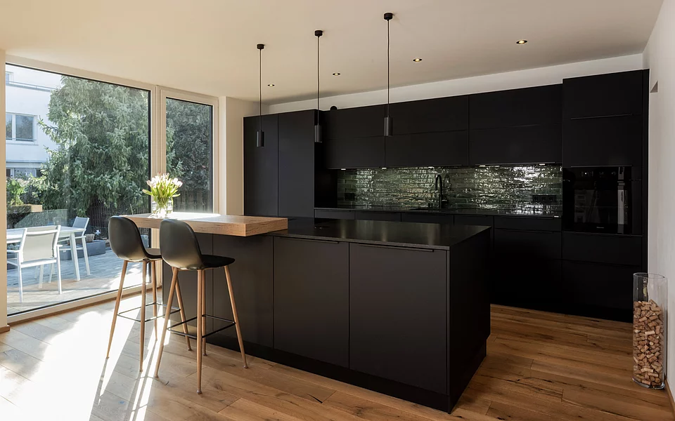 Elegante Küche mit schwarzen Hochglanzfronten und Kochinsel, umgesetzt vom Küchenstudio Lorinser