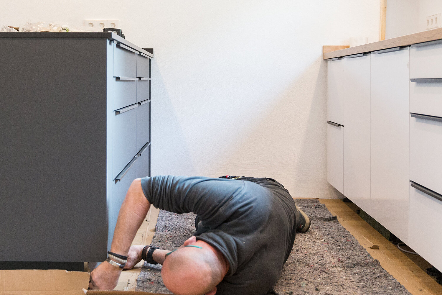 Mitarbeiter von Lorinser liegt seitlich auf dem Boden und montiert Fußleiste einer Küche