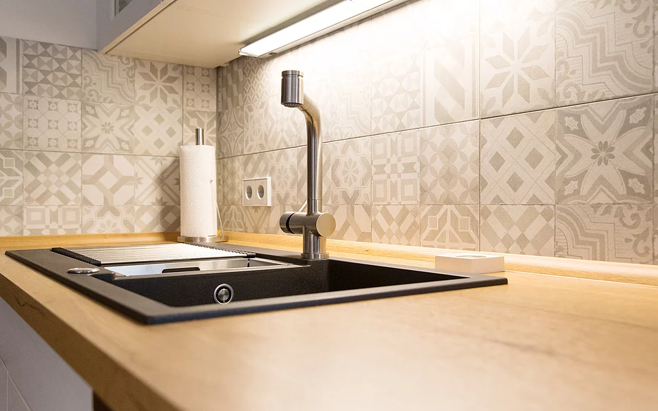 Küche mit heller Arbeitsplatte, Spüle und strukturierter Nischenrückwand, umgesetzt vom Küchenstudio Lorinser