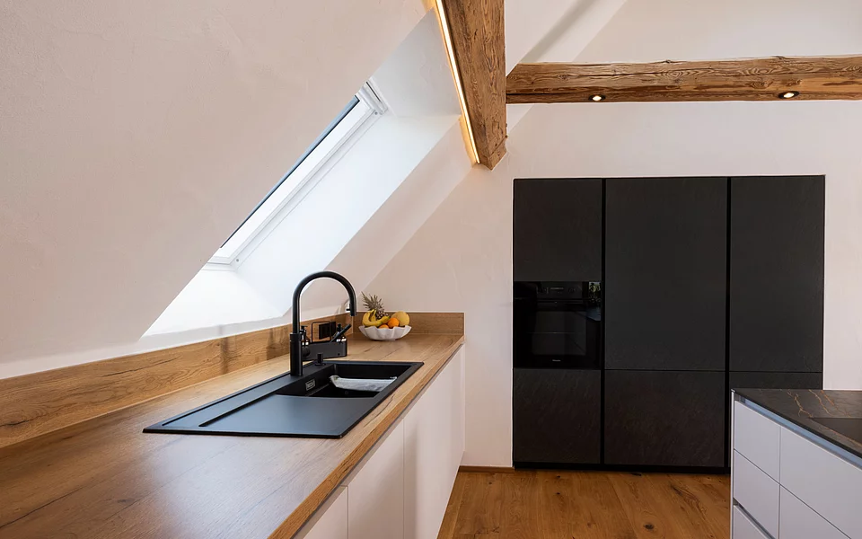 Kleine funktionale Küche unter Dachschräge mit clever genutztem Stauraum, geplant vom Küchenstudio Lorinser