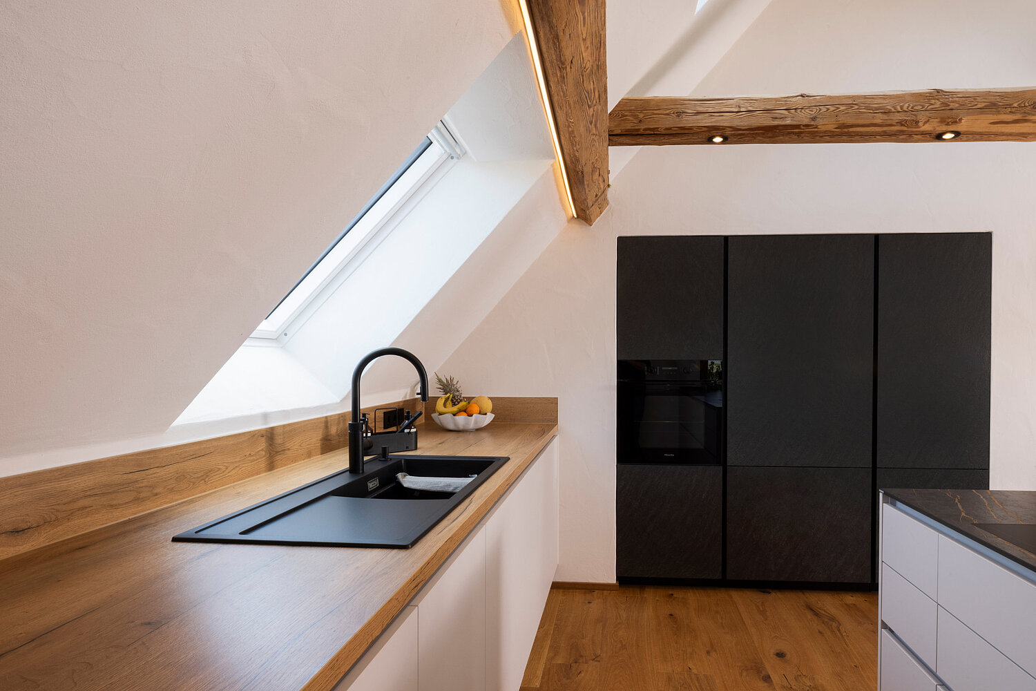 Kleine funktionale Küche unter Dachschräge mit clever genutztem Stauraum, geplant vom Küchenstudio Lorinser