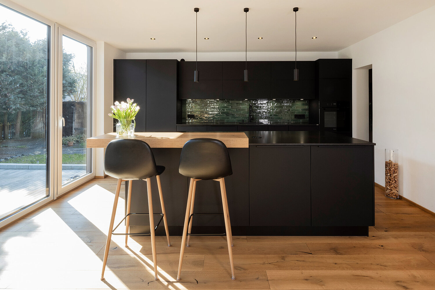 Moderne Küche mit dunklen Fronten, Essbereich und stilvoller Beleuchtung, realisiert vom Küchenstudio Lorinser