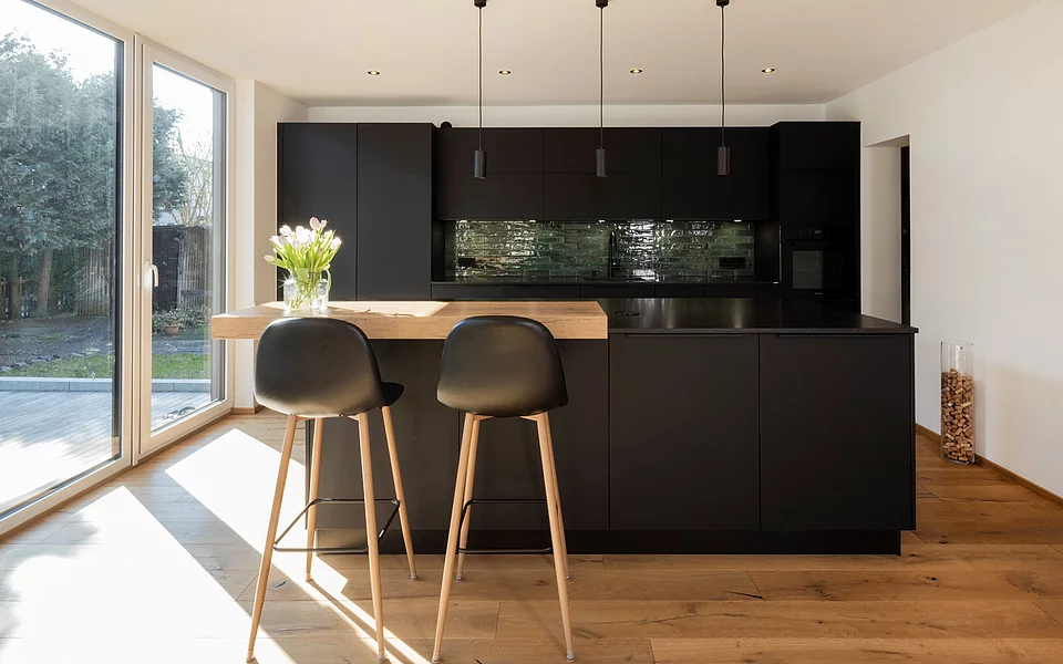 Moderne Küche mit dunklen Fronten, Essbereich und stilvoller Beleuchtung, realisiert vom Küchenstudio Lorinser